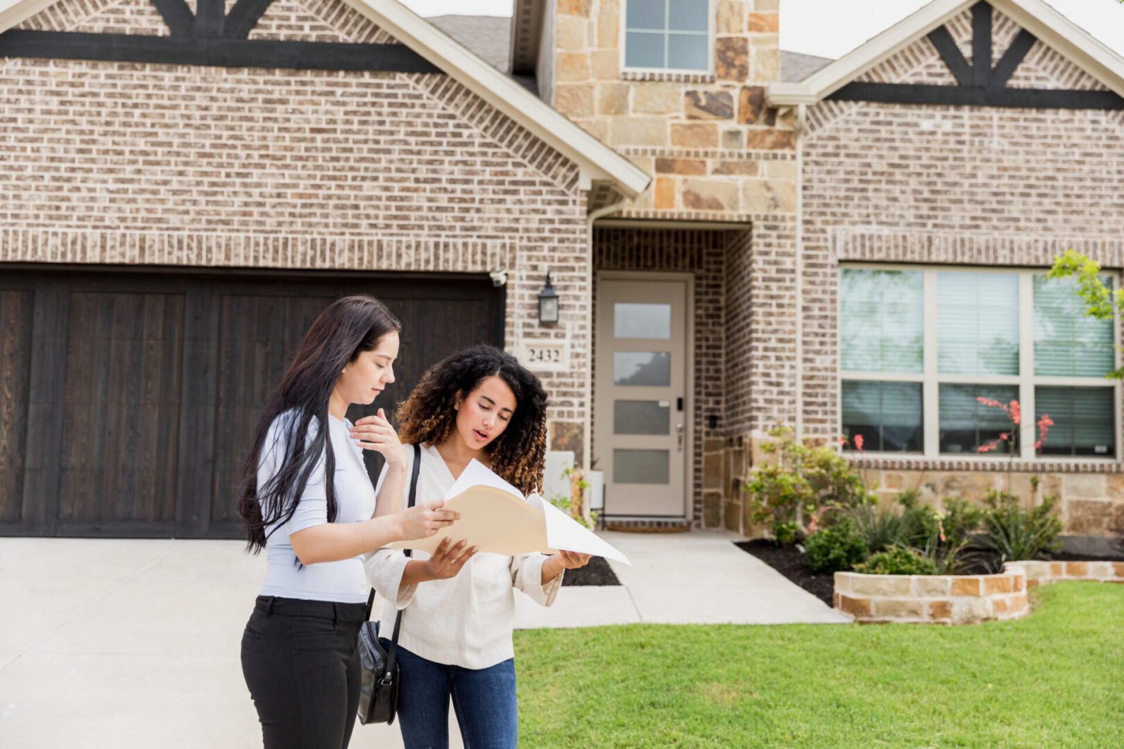 Two women discussing paperwork outside a house.